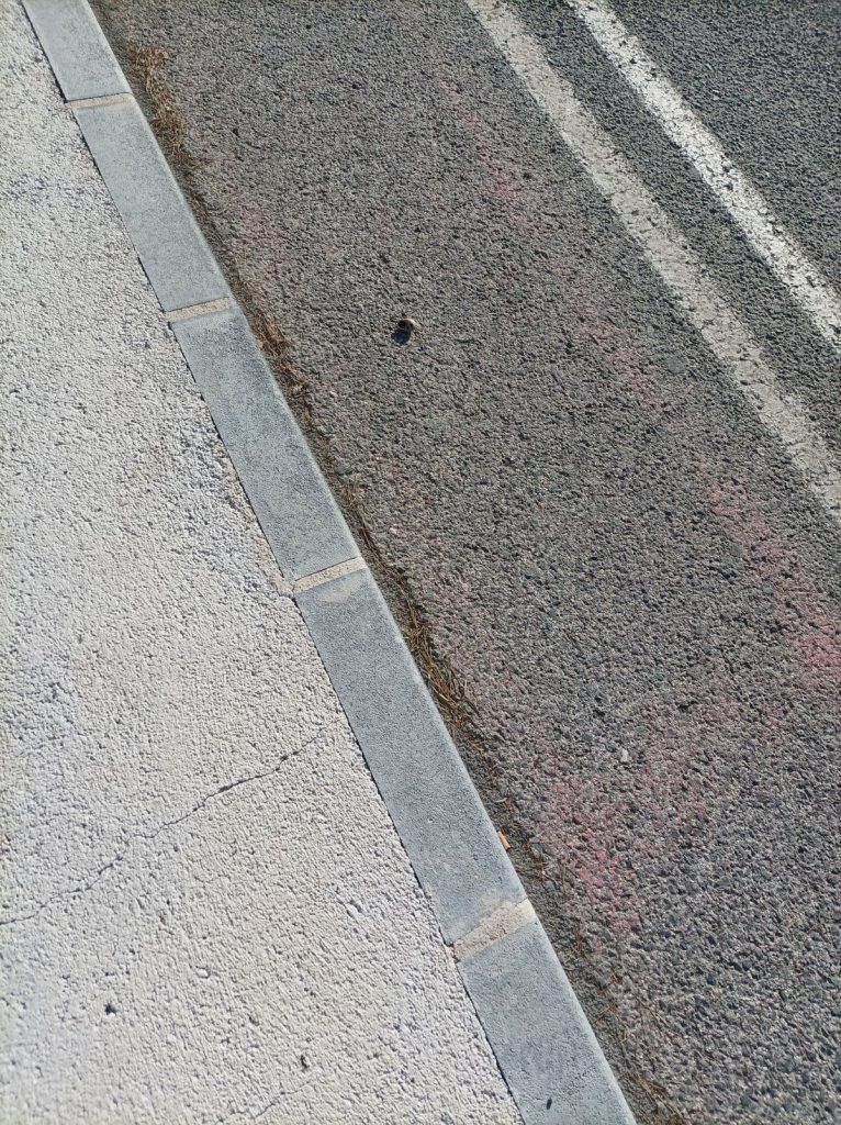 Concrete curb separating sidewalk from street showing typical curb and gutter structure in an urban setting