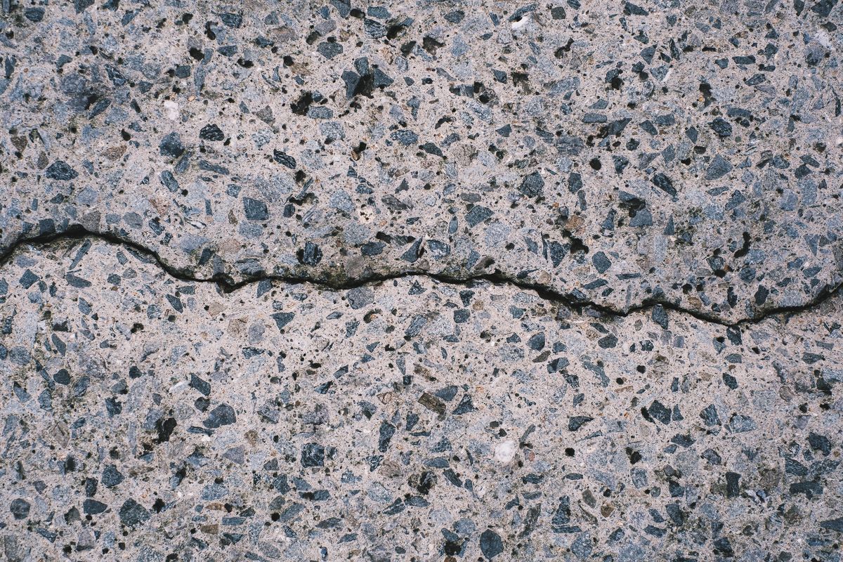 Close-up of cracked and deteriorating concrete surface showing aggregate exposure and structural damage
